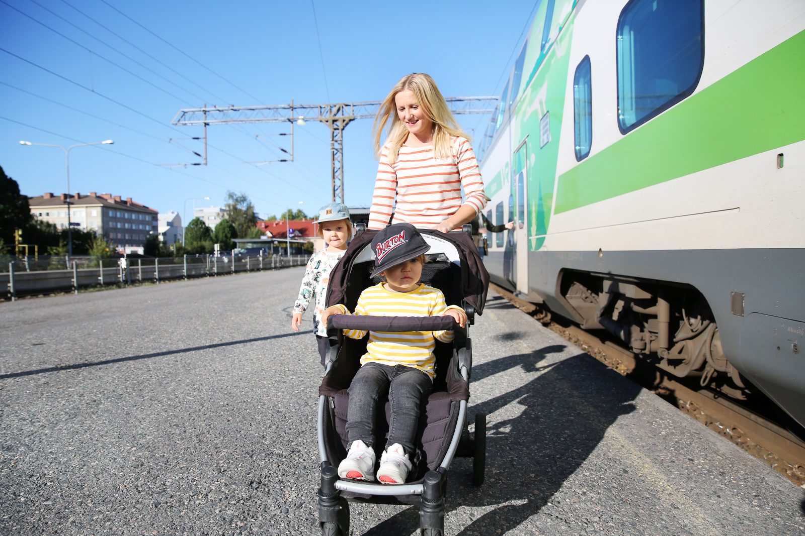 Nainen lastenrattaiden ja kävelevän pikkulapsen kanssa rautatieasemalla Oulussa.