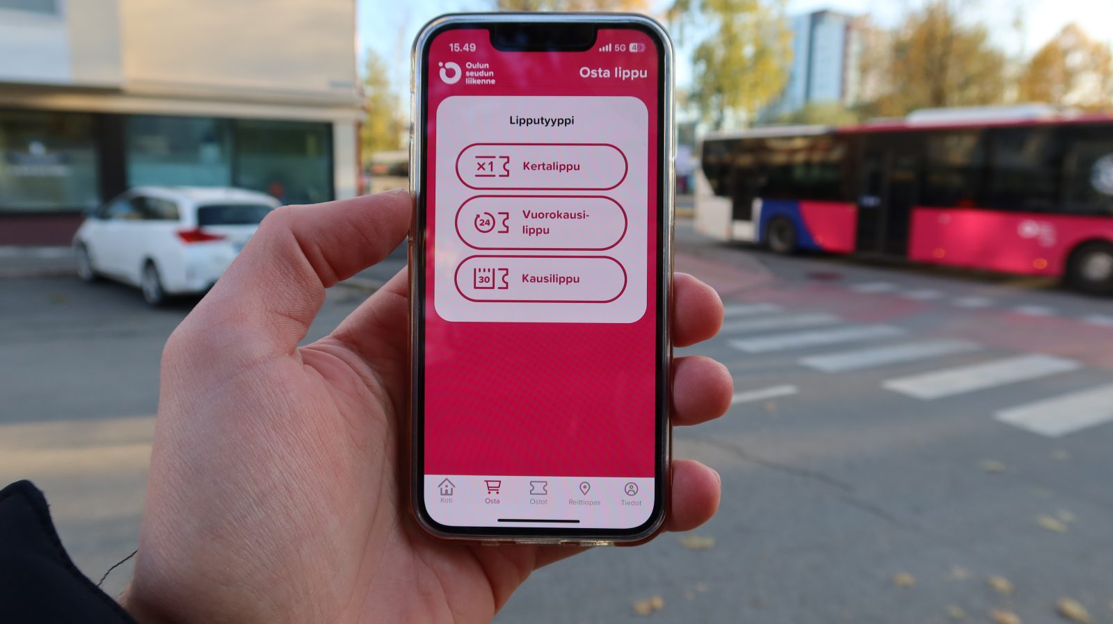 Matkapuhelin kämmenellä ja taustalla bussi.