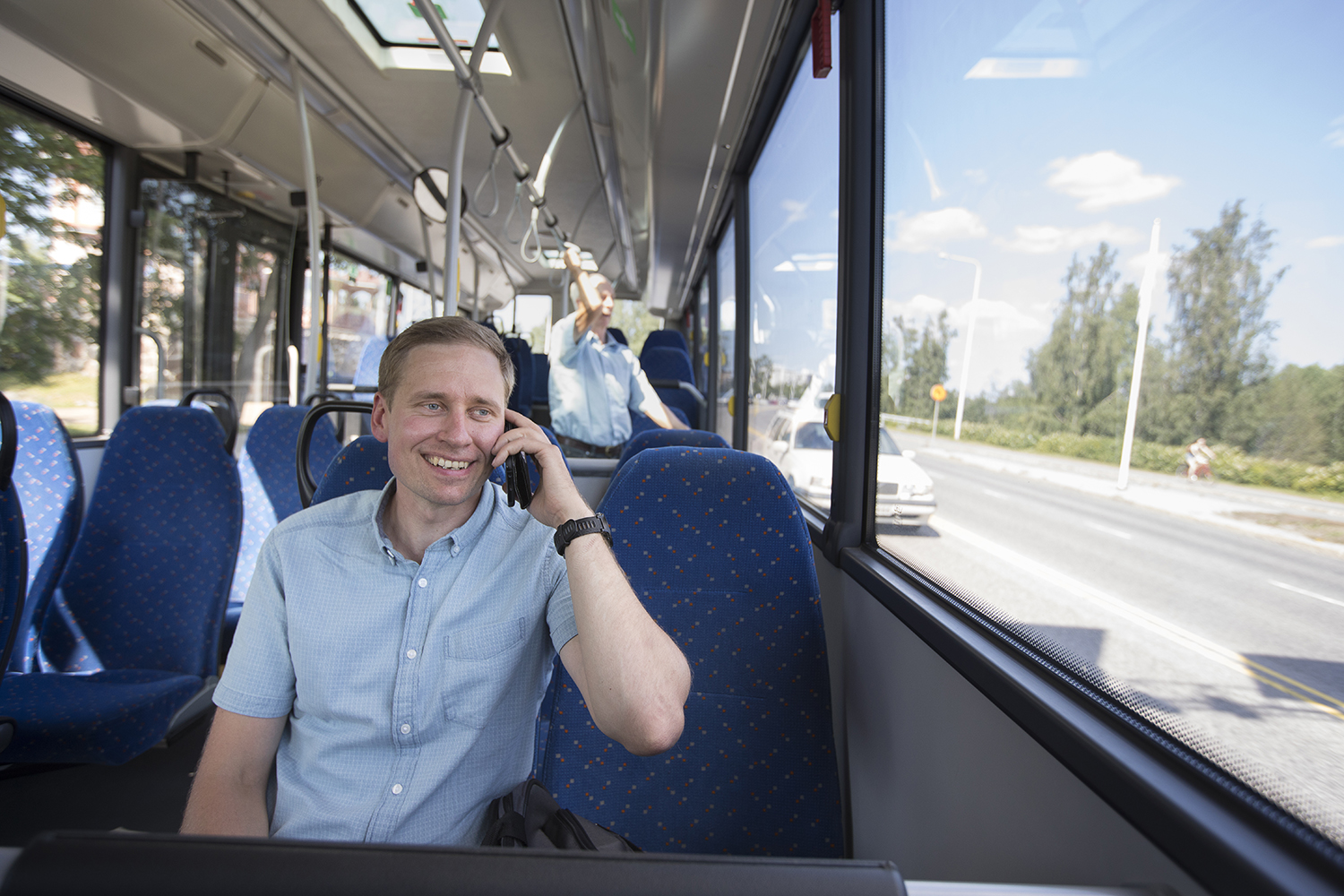Mies istuu bussissa ja puhuu puhelimeen.
