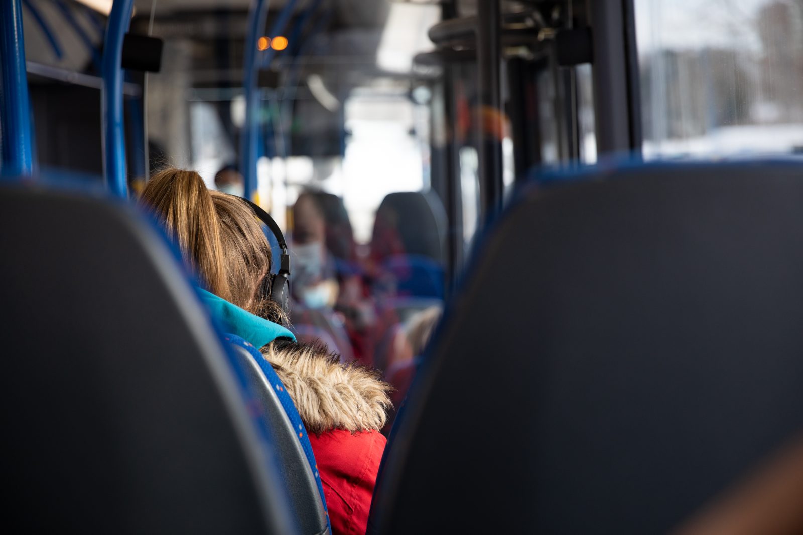 Matkustajia istumassa bussissa toppatakit päällä.