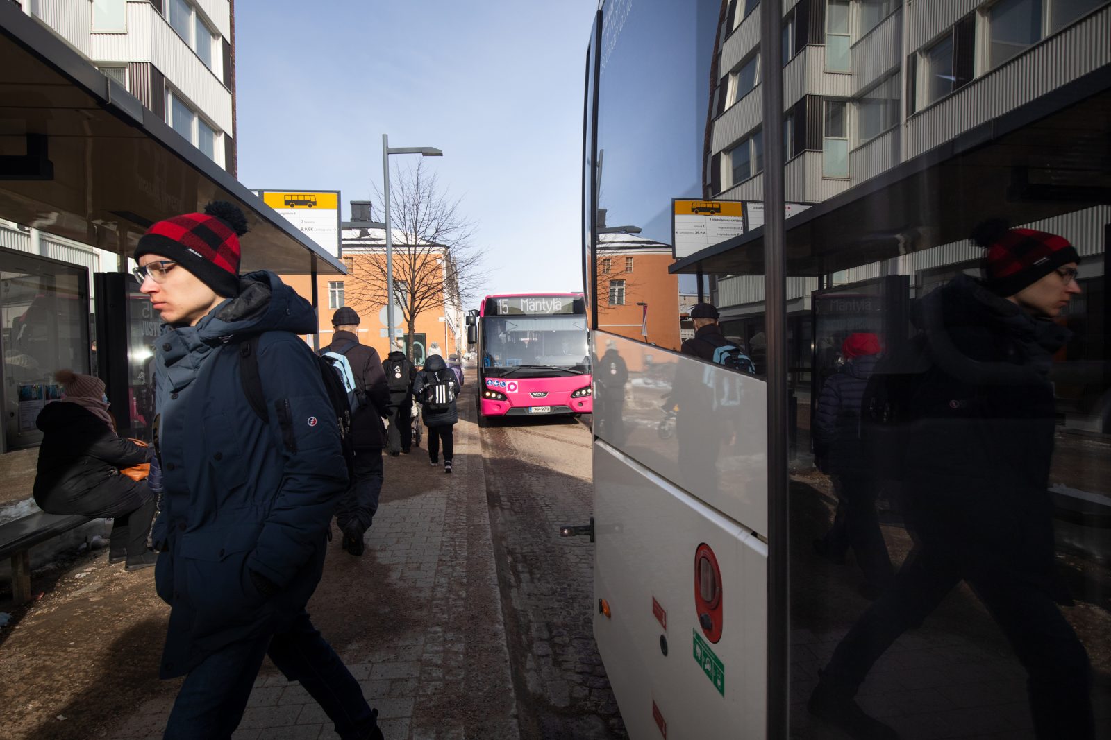 Talvella bussipysäkillä matkustajia ja lähtevä ja saapuva bussi.
