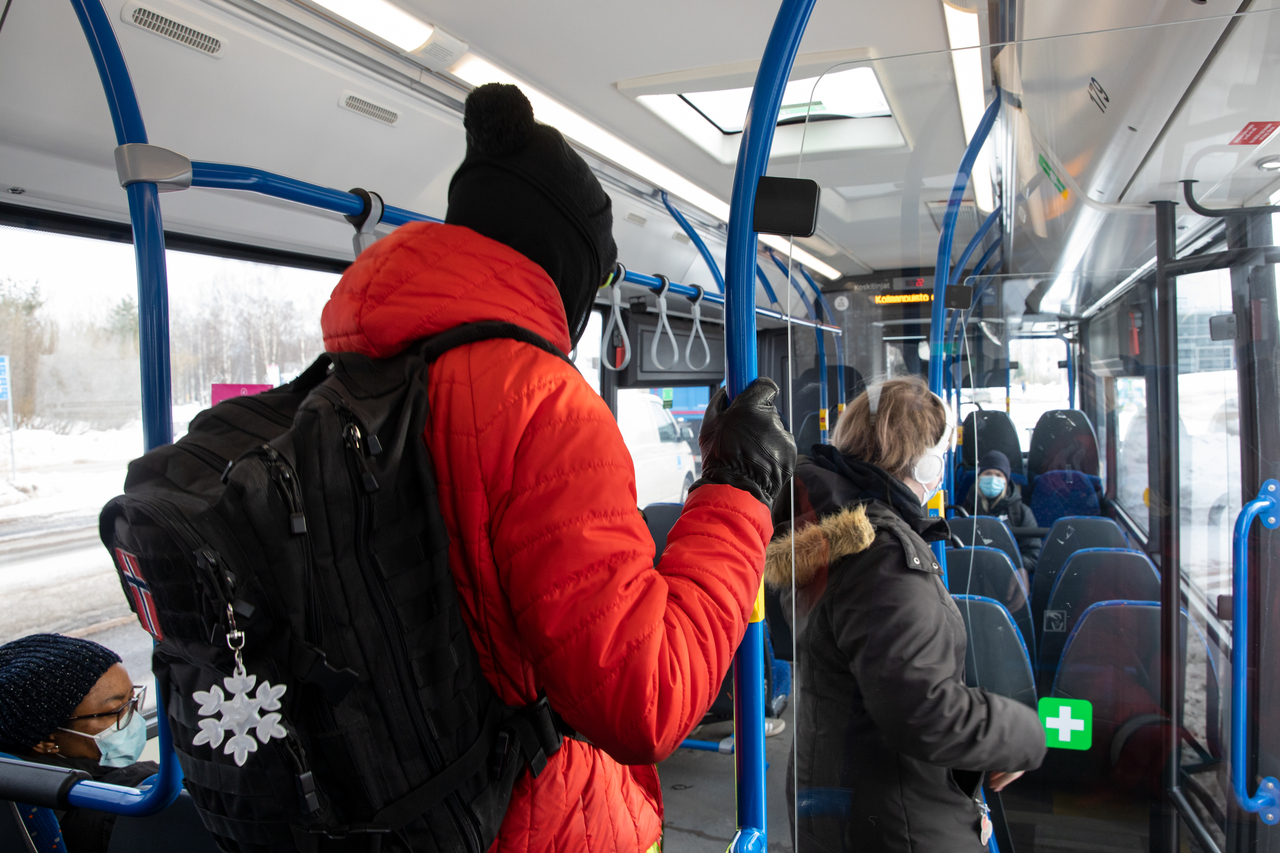 Matkustajia bussissa talvivaatteissa selin kuvaajaan.