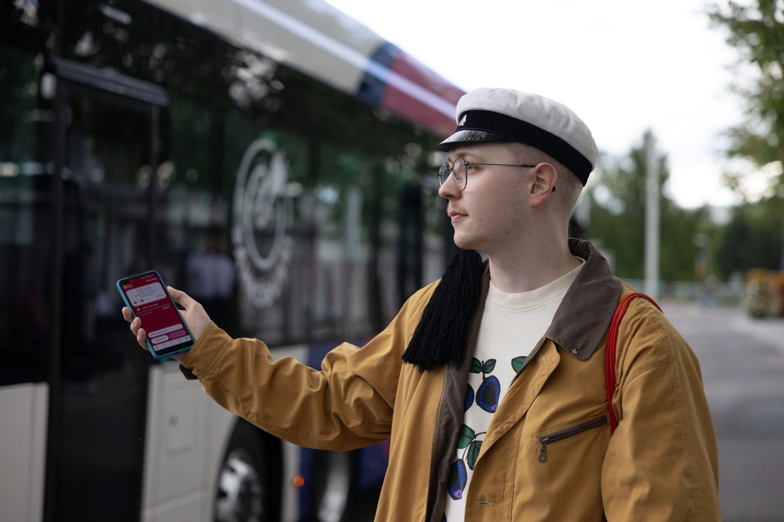 Opiskelija kännykkä kädessä bussipysäkillä.